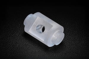 Precision-machined custom sapphire part with a central hole, displayed in close-up on a dark background.