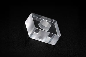 Transparent sapphire cube with an internal cylindrical feature, showcasing complex geometry in a custom sapphire part.