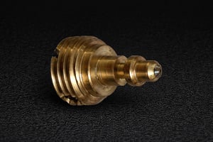 Precision brass fitting with stepped threads and central bore, manufactured to accommodate a custom sapphire part.